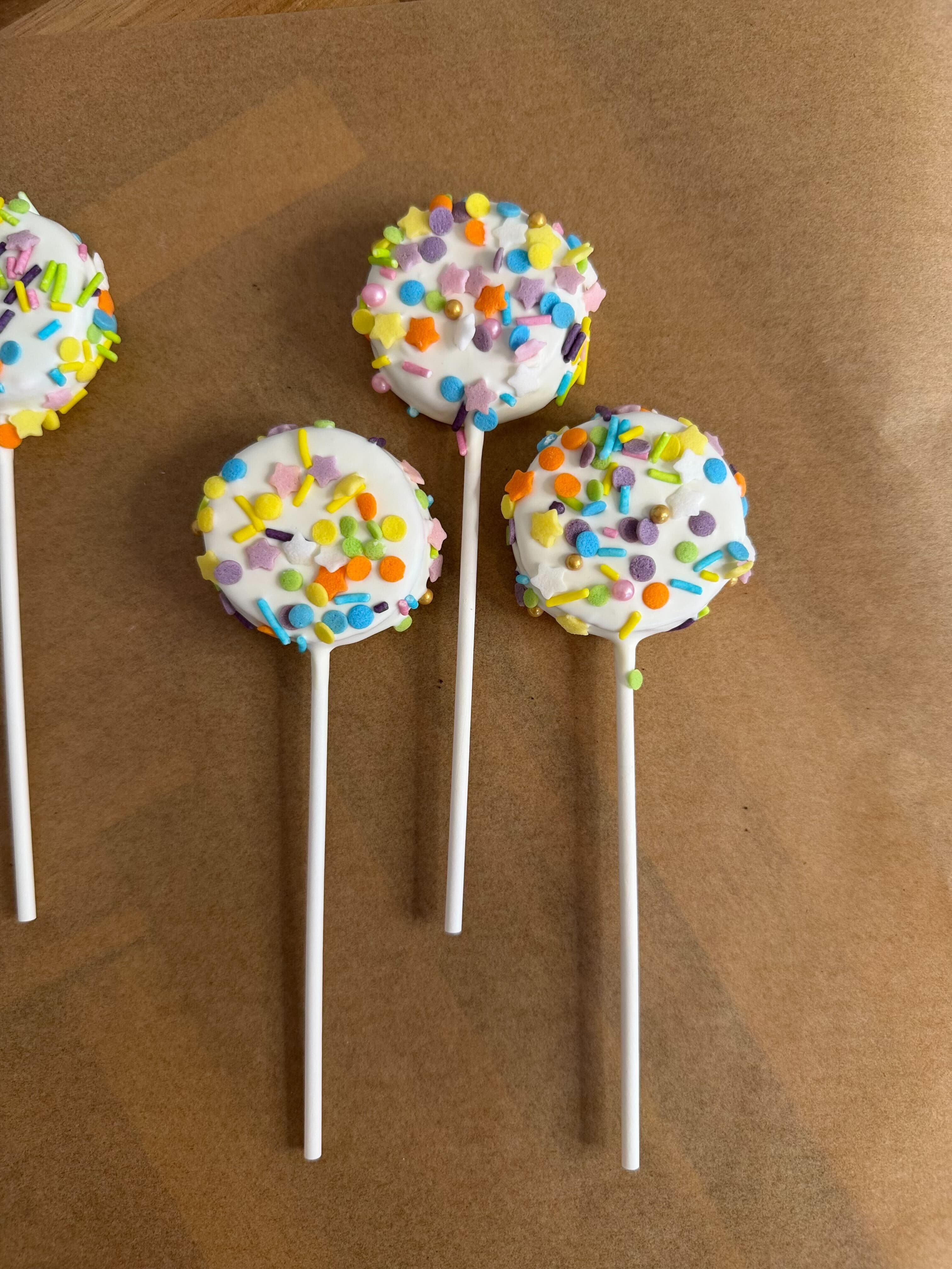 Colorful cake pops coated in white chocolate with vibrant rainbow sprinkles