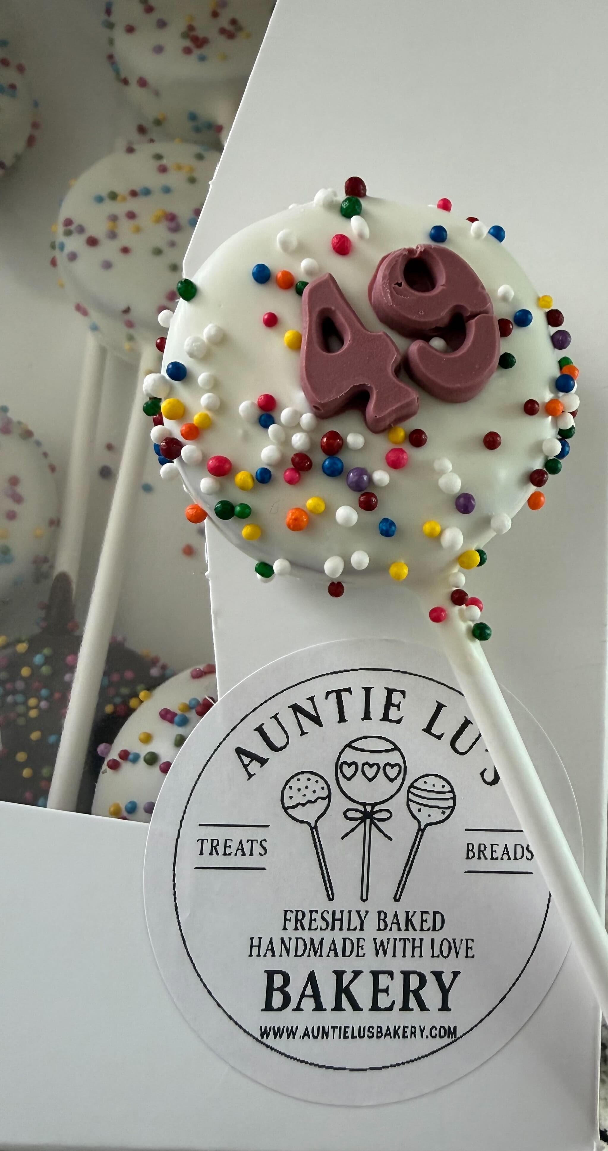 White chocolate cake pop with rainbow sprinkles and a "49" number topper