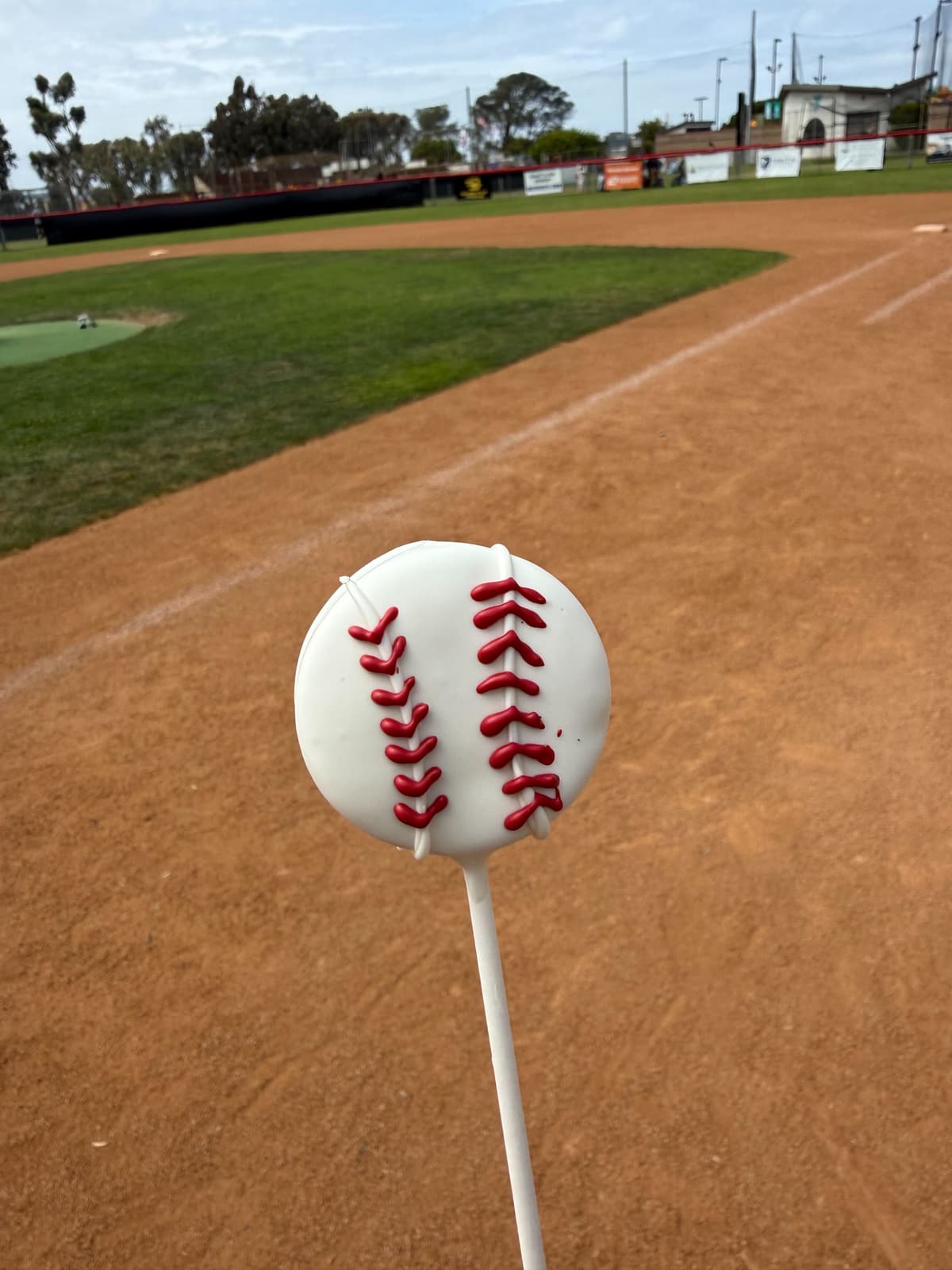 Custom baseball cake pop with red stitching on a sunny ballfield