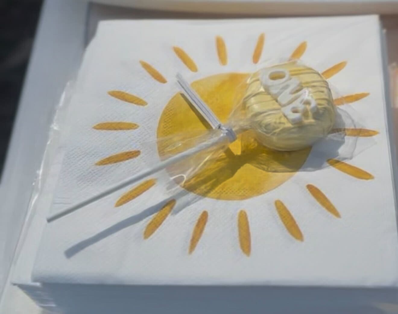 Wrapped yellow 'ONE' first birthday cake pop favor on a sunshine napkin